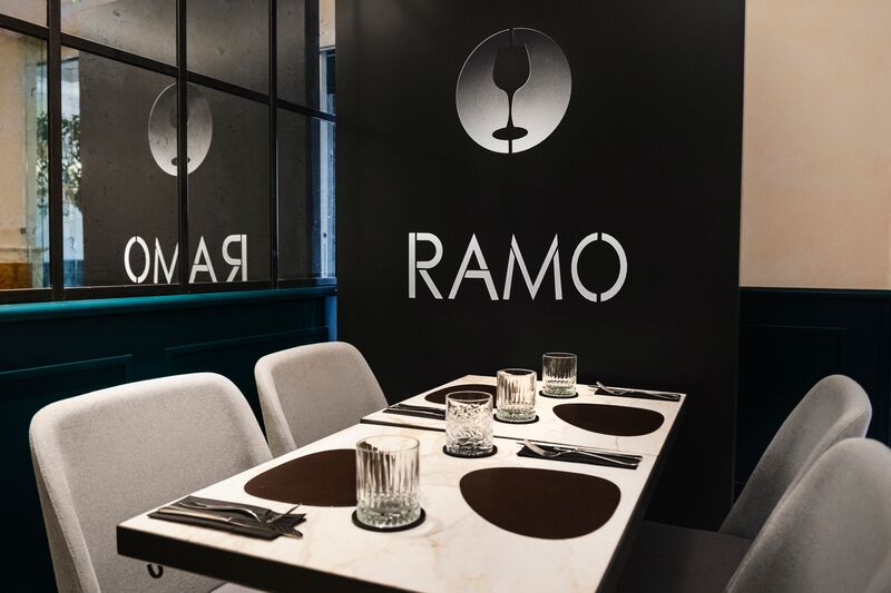 Tavolo in marmo bianco apparecchiato davanti alla parete nera con il logo RAMO